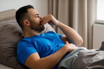 Sick Arab man suffering from runny nose and sore throat. lies in bed, blows his nose and sneezes into a paper napkin, a banner.