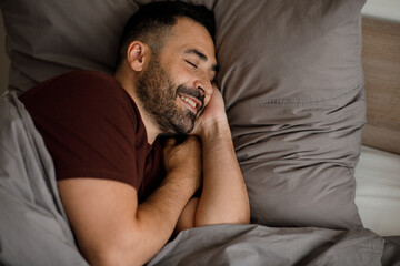 Happy man wakes up in the morning in a good mood in a gray bed