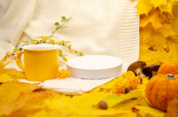 Autumn still life in yellow-orange tones: a white knitted plaid and leaves, empty podium  white...