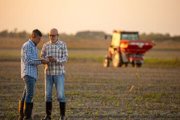 Two farmers in field with tractor in background