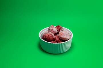 Closeup of frozen strawberries in a bowl isolated on green background