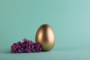 Easter egg painted in gold color decorated with purple lilac floewrs. Happy Easter minimalistic background.
