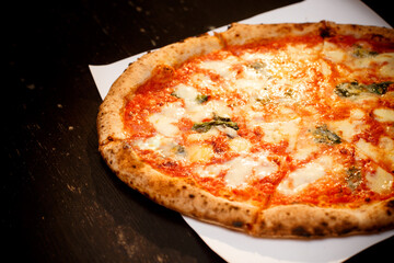classic pizza with cheese baked in the oven. Pizza on a white sheet of paper and on a black background. Photo for the pizzeria menu.