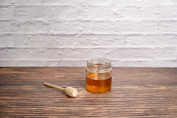 Pot of honey and wooden stick isolated white brick wall