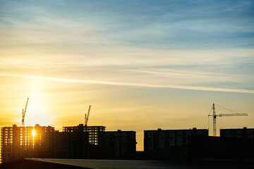 Group of tower cranes on the construction site against sunset eveninng sky. Silhouette of real estate construction. Real estate construction. Concept of urban development and architecture.