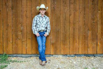 Young cowboy leaning back against the side of a horse barn