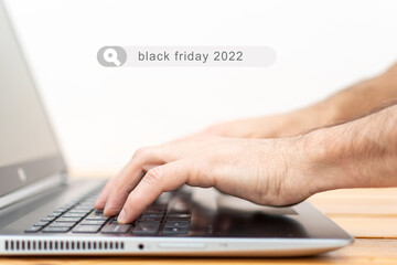 Hands looking for black friday 2022 on a laptop keyboard.