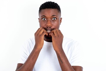 Anxiety - young handsome man wearing white T-shirt over white background covering his mouth with hands scared from something or someone bitting nails.