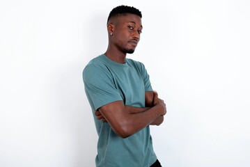 Waist up shot of  self confident young handsome man wearing green T-shirt over white background has broad smile, crosses arms, happy to meet with colleagues.