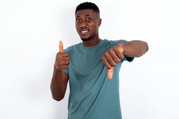 young handsome man wearing green T-shirt over white background feeling unsure making good bad sign....