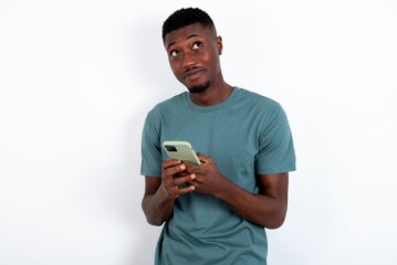 Happy young handsome man wearing green T-shirt over white background listening to music with earphones using mobile phone.