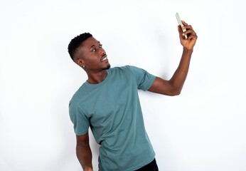 Portrait of a young handsome man wearing green T-shirt over white background taking a selfie to...