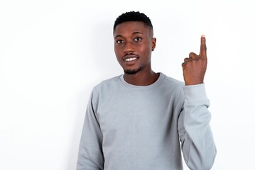young handsome man wearing grey sweater over white background smiling and looking friendly, showing number one or first with hand forward, counting down