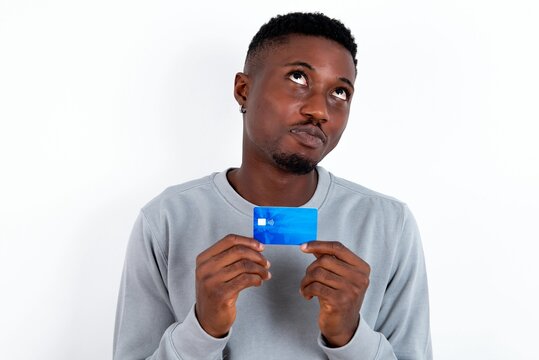 Photo of cheerful young handsome man wearing grey sweater over white background hold debit card look empty space