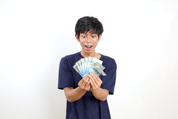 Surprised young asian man standing while holding Indonesian banknotes. Isolated on white