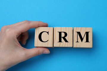 Woman making abbreviation CRM of wooden cubes on blue background, closeup. Customer Relationship...