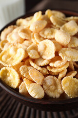 Bowl of tasty crispy corn flakes on wooden board, closeup