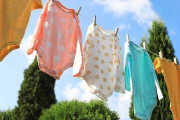 Clean baby onesies hanging on washing line outdoors. Drying clothes