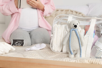 Pregnant woman preparing list of necessary items to bring into maternity hospital in bedroom, focus on bag and toy