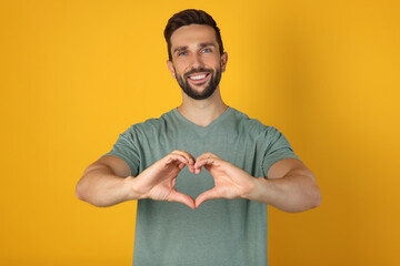 Happy man making heart with hands on yellow background