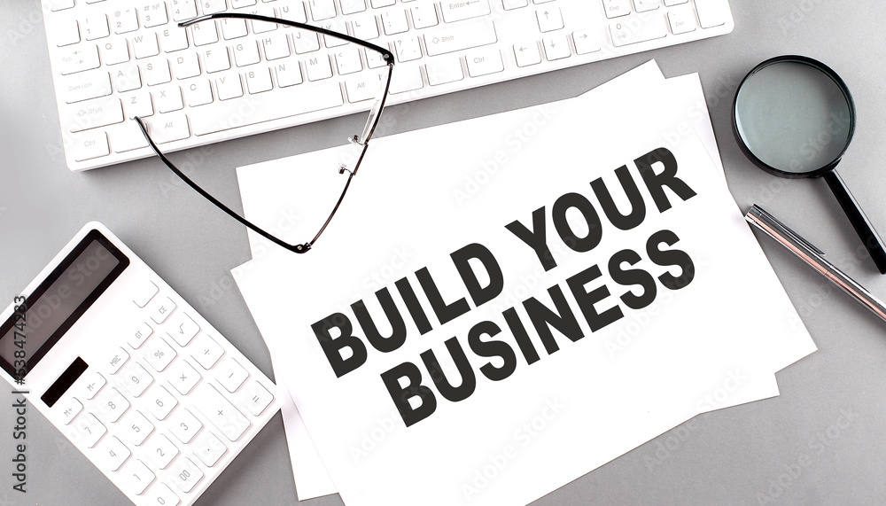 Poster build your business text on a paper on a gray background near a calculator and a white keyboard