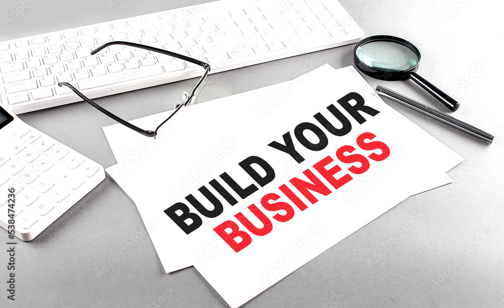 Poster build your business text on a paper on a gray background near a calculator and a white keyboard