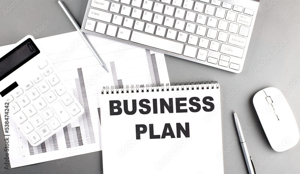 Poster business plan text written on notebook on grey background with chart and keyboard , business concept