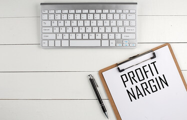 Home office workspace with keyboard, clipboard and pen with text PROFIT MARGIN on white wooden...