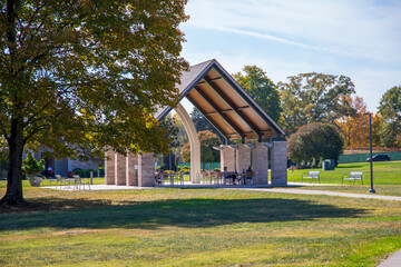 a gorgeous autumn landscape at Lakeshore Park with a brown wooden and stone pergola surrounded by autumn colored trees and lush green trees and grass with blue sky and clouds in Knoxville Tennessee - obrazy, fototapety, plakaty