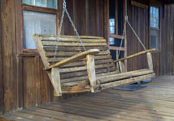 Fototapeta na wymiar Chain suspended old wooden porch swing on porch - extended view