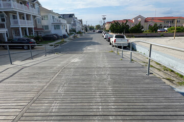View down a wooden plank boardwalk ramp to an asphalt street in a beach town