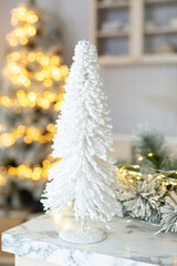 Small decorative stylish artificial Christmas fir-tree on a table on background of garland lights. Vintage New Year decorations. Gift boxes  under fir-tree. Christmas mood. Celebrating of New Year