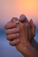 newly engaged couple holding hands with engagement ring on finger and sunset in the background