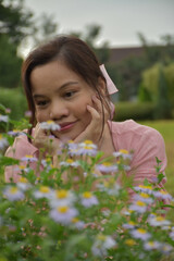 A woman sits and looks at real flowers in the middle of nature, looking like an outdoor flower garden.
