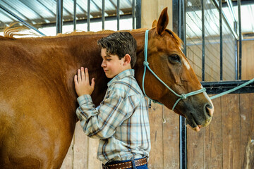 Young boy petting or grooming his horse in the stable