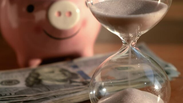 Close up timeglass, banknote and piggy bank on wooden table. Saving money concept.