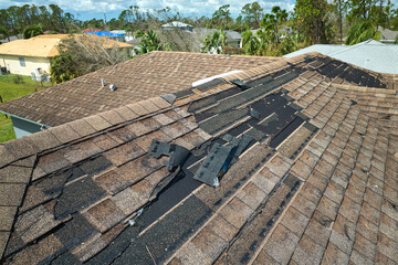 Wind damaged house roof with missing asphalt shingles after hurricane Ian in Florida. Repair of...