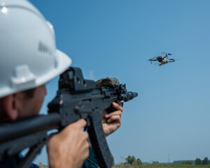 Caucasian man in a helmet shoots a flying drone with a rifle. 