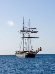 Tall ship at anchor on blue ocean against blue sky