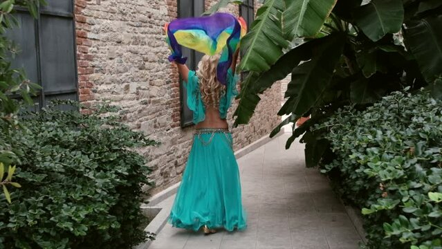 belly dancer woman flies her colorful fabric and walks among ancient builds and tropical plants in slow motion