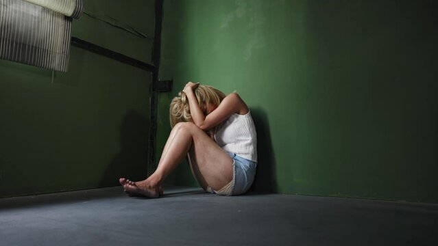 The abducted woman's wrists and feet are bound in red rope, with no way to fight or resist. Female hostages require assistance. Woman with issues sitting on the floor in the room as a hostage idea