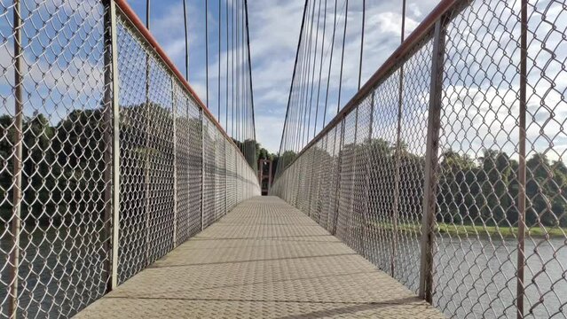 Hanging suspension bridge architecture made with join iorn metal cable rope and tower for crossing green forest river water. Empty and quiet endless deck, walkway or path close up view during daytime.