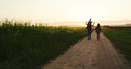 Family walking along a farm at sunset, bonding and having fun in nature. Agriculture, happy family and peaceful walk along a field of grass with parents and child talking, relaxing and enjoying view