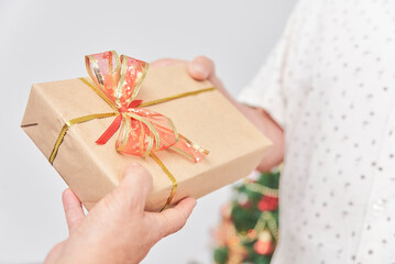 Unrecognizable adult couple spending the holidays together at home, one gives a Christmas gift to the other. Close-up image, focus on the giftbox, wrapped and decorated with a ribbon bow.