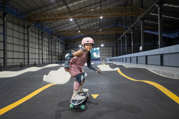 asian child skater or kid girl fun playing skateboard or ride surf skate in indoor pump track in...