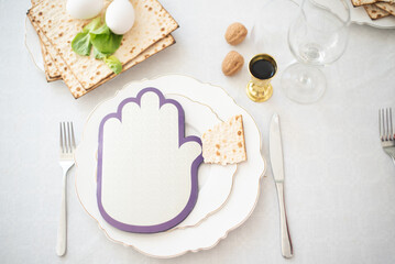 Close_up of festive table on white tablecloth: cutlery, matzah, book, eggs, salad. Traditional of Jewish Holiday on Passover. Home symbol of lovely family. top view, layout. love and care.