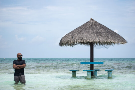 A picture of an Indian guy sitting under a hut in the shallow sea of Maldives and enjoying his vacation 