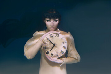 Gothic Spooky woman with clock in her hands in black veil underwater