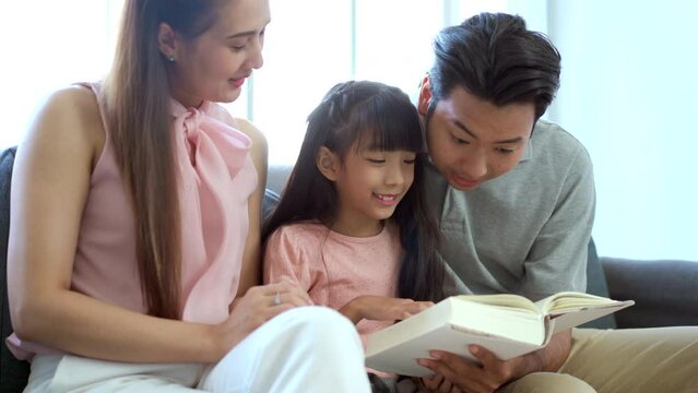 family spending a time together during a free time in weekend. Father, mother, and their daughter relaxing and reading a book or novel together in the living room.