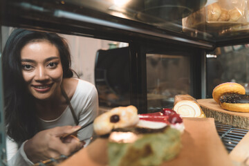 beautiful waitress pick a donut from customer order and put a donut on a plate and present bakery and give to customer. the happiness woman in bakery small business on waitress uniform.